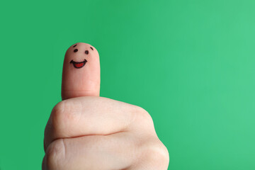 Finger with happy face drawing on green background. Space for text