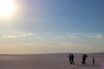 Silhouettes of people walking on Salt Lake. Bright sun and cloudy sky. Selective focus.