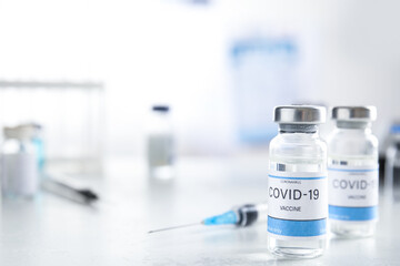 Vials with vaccine against Covid-19 and syringe on white table indoors. Space for text