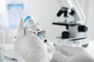 Doctor filling syringe with vaccine against Covid-19 indoors, closeup