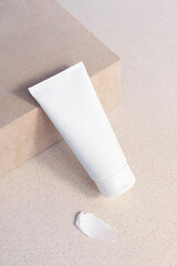 white cosmetic tube with face or hand cream, cleanser or body lotion with cream swatch on a beige sand background, leaning against a suede box. Gentle skin care concept. Copy space