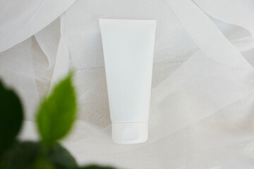 white cosmetic tube for face cream, body lotion or face cleanser on draped fabric with delicate...