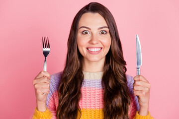 Portrait of attractive cheerful funny brown-haired girl holding in hands fork knife ready to have...