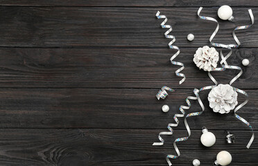 Flat lay composition with serpentine streamers and Christmas decor on black wooden background. Space for text