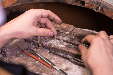 A male jeweler makes repairs to a gold chain at his workplace