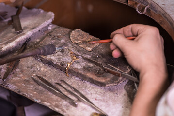 A male jeweler makes repairs to a gold chain at his workplace