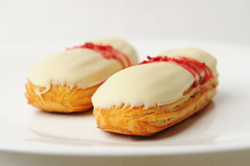 French dessert eclair with vanilla cream and strawberry sauce on white plate. Elegant serving style