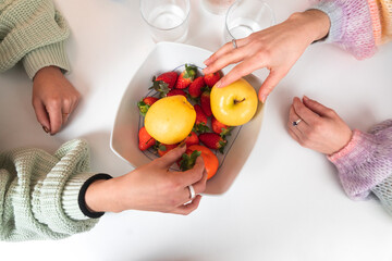 Two female hands taking fruits from a ball on a table