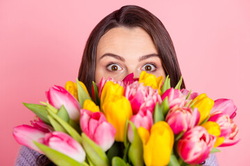 Fototapeta premium Close-up portrait of attractive funny amazed girl holding bunch tulips hiding isolated over pink pastel color background