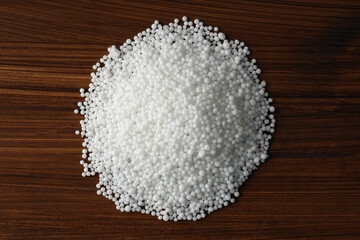 Pellets of ammonium nitrate on wooden table, flat lay. Mineral fertilizer