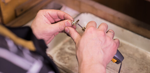 Hands of a jeweler who grinds a silver chain with a cross
