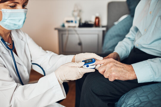 Doctor measuring the degree of oxygen saturation of the blood and heart rate of senior patient using pulse oximeter. Home treatment of virus. Checking health condition. Coronavirus pandemic. Covid-19