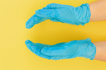 Doctor's hand in blue medical  (surgical) gloves holds abstract object on yellow background. Place for your product.