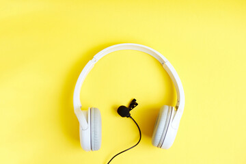 Background with headphones and clip-on microphone on yellow background, flat lay. Top view. Audio...