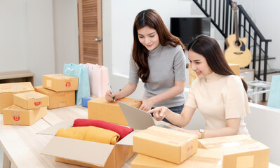 Fototapeta na wymiar Two beautiful Asian women are checking orders by laptops via the internet. And pack the paper box With a happy smiling face, being a new normal online business