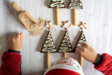 Overhead view of little child with Santa hat decorating the home made chocolate brownies and cookies in shape of Christmas tree