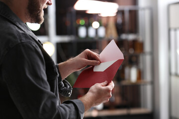 Man holding envelope with greeting card indoors, closeup