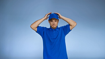 discouraged delivery man holding hands over head isolated on blue