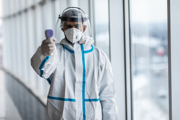 Medical man worker scanning with infrared thermometer, IR Thermoscan. Confident Asian doctor in protective PPE suit wearing face mask and eyeglasses in hospital