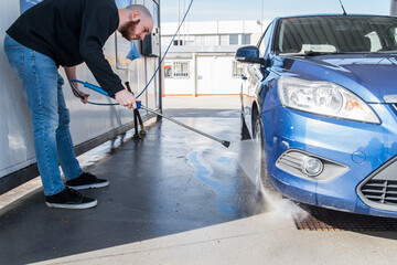 Concepto de lavado de coches. Hombre usando agua a alta presión para limpiar un neumático de su coche. Lavado de ruedas del coche