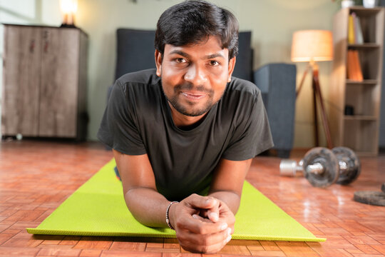Young Man With Smiling Face On Yoga Mat At Home After Working Out Looking Camera, Concept Of Home Gym, New Normal Lifetyle, Health And Fitness.