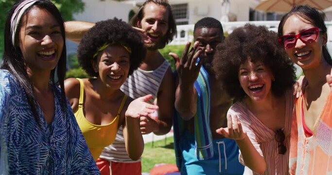 Portrait of diverse group of friends smiling and waving to camera at a pool party