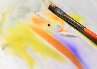 Paint brush on surface of mirror and splashes of colorful watercolor paints.Impressionist abstract...
