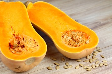 Pumpkin Butternut Liscia cut in half. Yellow delicious pumpkin on wooden table, seeds around.