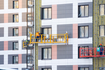 Finishing the facade of residential buildings by workers on the construction elevator, completion...
