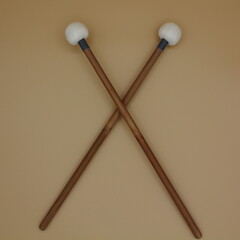 Crossed timpani mallets on a cream background.