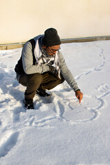 Fototapeta na wymiar Person sitting in the snow and drawing a heart with a smiling face in the snow during winter time. 