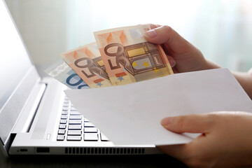 Envelope with euro banknotes in female hands. Woman pulls money out of an envelope on laptop background, wages, bonus or bribe concept - obrazy, fototapety, plakaty
