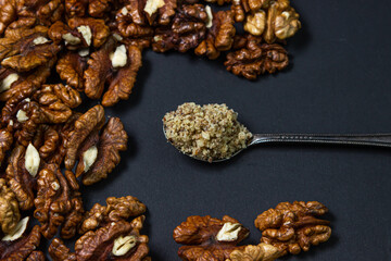Peeled walnuts and ground walnuts on a black background. A wooden spoon full of ground walnuts. Nutritious food