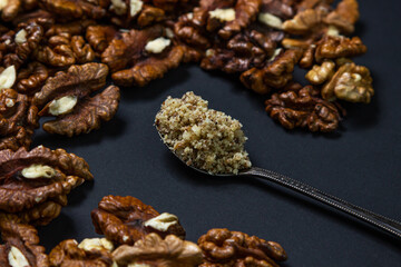 Peeled walnuts and ground walnuts on a black background. A wooden spoon full of ground walnuts. Nutritious food