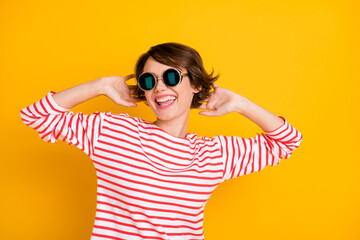 Photo of young beautiful positive excited smiling cheerful girl in sunglasses dancing isolated on yellow color background
