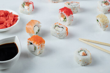 Sushi rolls mixture on a white background with soy sauce and red ginger