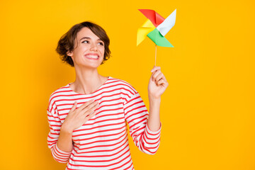 Photo of young attractive beautiful positive cheerful smiling dreamy girl with pinwheel isolated on yellow color background