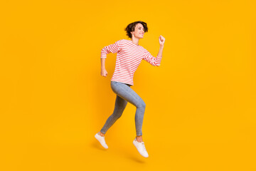 Fototapeta na wymiar Full size profile photo of optimistic brunette lady run jump wear red shirt jeans sneakers isolated on orange color background