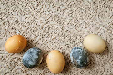 Easter eggs lie in a semicircle on a beige lace tablecloth. Copy space