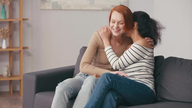 interracial lesbian couple hugging and smiling in living room
