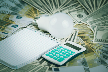 LED light bulb and money. Banknotes dollars and euros are laid out on the table. Energy-saving concept.