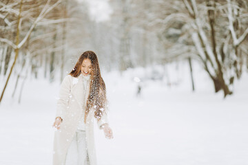 Winter portrait of a merry young woman playing with snow at the park