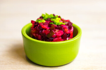 Homemade Russian beet salad vinegret in green bowl on white table background