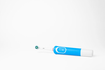 Blue modern electric toothbrush lying on a white background, copy space. Controlled tool for daily oral care.