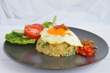 Nasi goreng or Indonesian fried rice with egg garnished with  lettuce, fresh cucumber slices , slice tomato, sambal, and sunny side up 