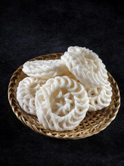 Kerupuk putih or kerupuk warung is Indonesian traditional deep fried crackers made from starch mixed with flavorings such as fish, served in wicker plate. Isolated against black background.