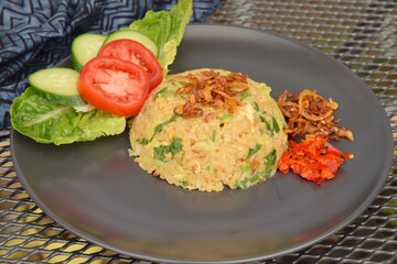 Nasi goreng or Indonesian fried rice with egg garnished with  lettuce, fresh cucumber slices , slice tomato, fried onion and sambal