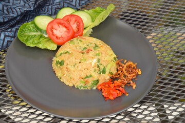 Nasi goreng or Indonesian fried rice with egg garnished with  lettuce, fresh cucumber slices , slice tomato, fried onion and sambal
