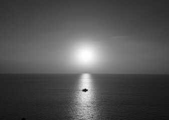 Photos of the boat on the ocean in the evening. Sunshine on water as glistening light with black and white color.  There is a horizon line behind. The idea for monochrome background with copy space.