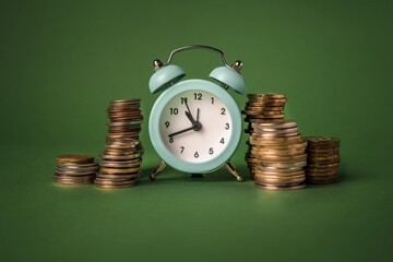 Alarm clock and stacks of coins on a green background. The concept of value time is money. A symbol of money accumulation.
